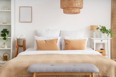 Yumuşak yastıklı rahat bir yatak ve açık renk yatak odasında bej bir battaniye