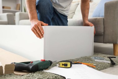 Genç adam, rafları halıya diziyor, yakın plan.