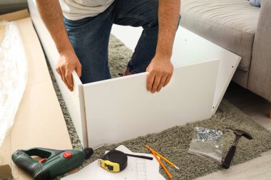 Genç adam evdeki halının üzerine raf monte ediyor.