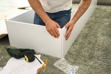 Genç adam evdeki halının üzerine raf monte ediyor.