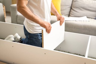 Genç adam raf ünitesini evde monte ediyor.