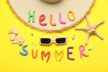 Yazılı Hello YAZ kompozisyonu, şık plaj aksesuarları ve sarı arka planda deniz yıldızı
