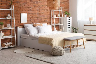 Yatak odasının içinde rahat yatak odası, yatağın yanında bank ve raf üniteleri var.