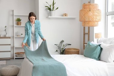 Güzel genç bir kadın hafif yatak odasında yatağını yapıyor.