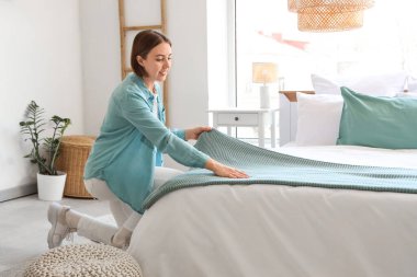 Güzel genç bir kadın hafif yatak odasında yatağını yapıyor.