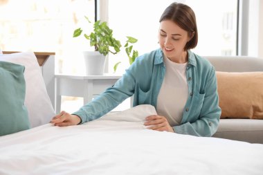 Güzel genç bir kadın hafif yatak odasında yatağını yapıyor.