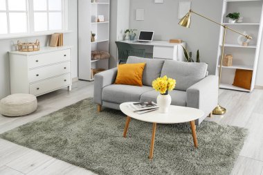 Gri kanepesi ve kahve masasında güzel narsisli çiçekleri olan şık bir oturma odası.