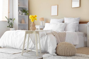 Şık bir yatak odası, rahat bir yatak odası ve komodinin yanında güzel narsisli çiçekler.