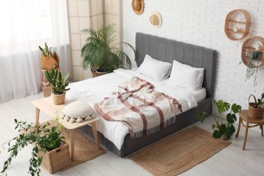 Yatak odasının içi bençle, katlanır ekranla ve hasır sepetlerde bitkilerle dolu.