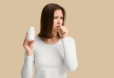 Bej arka planda haplar olan kavanozu tutan genç bir kadın.