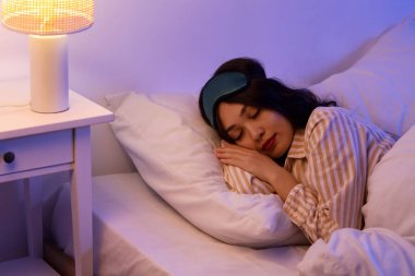 Uyku maskesi ve parlak lambasıyla geceleri uyuyan güzel genç bir kadın.
