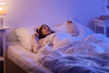 Uyku maskesi ve parlak lambasıyla geceleri uyuyan güzel genç bir kadın.