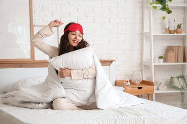 Evdeki yatakta uzanan uyku maskeli, yastıklı ve battaniyeli güzel bir kadın.