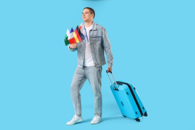 Farklı ülkelerden bayrakları ve renkli bir bavulu olan genç adam.