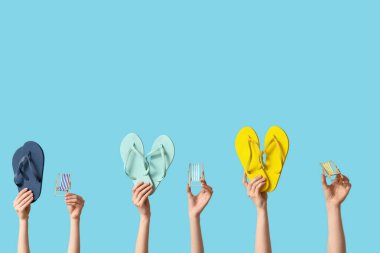 Mavi arka planda parmak arası terlikleri olan küçük güverte sandalyelerini tutan kadın eller.