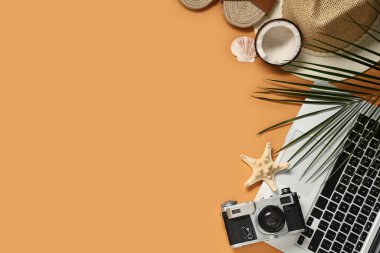 Kamera, şapka ve turuncu arka planda plaj dekoru olan dizüstü bilgisayar.