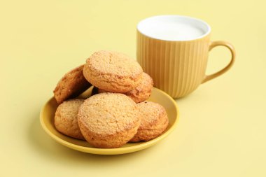 Tatlı kurabiyeli tabak ve sarı arka planda bir fincan taze süt.