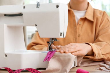 Atölyede kadın terzi fermuarı dikiyor, yakın plan.