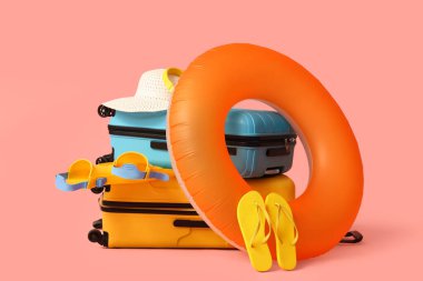 Bavullar, şişme yüzük, palet, hasır şapka ve pembe arka planda parmak arası terlikler.