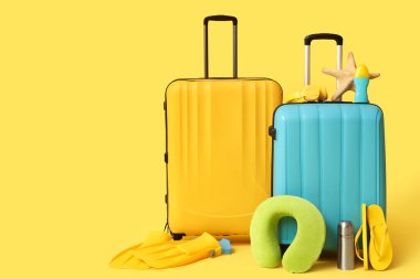 Sarı arka planda plaj aksesuarları, termos ve kulaklık olan bavullar.