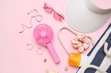 Kadın aksesuarları ve pembe arka planda mini fanı olan bir çanta.