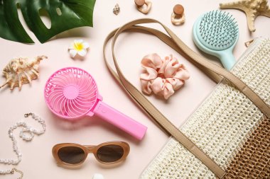 Kadın aksesuarları ve açık pembe arka planda mini fanı olan bir çanta.