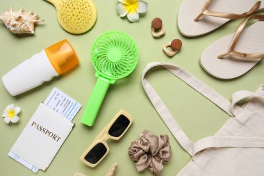 İçinde kadın aksesuarları, pasaport, bilet ve yeşil arka planda mini fan olan bir çanta.