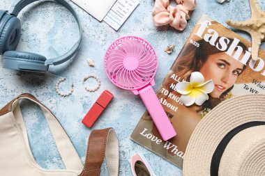 Mavi grunge arka planında kadın aksesuarları, kulaklıkları ve mini fanı olan moda dergisi.