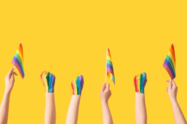 Sarı arka planda boyalı yumrukları ve LGBT bayrakları olan kadın elleri
