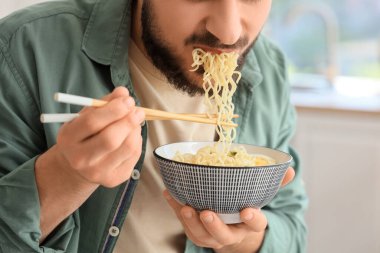 Genç adam mutfakta lezzetli ramen yiyor, yakın plan.