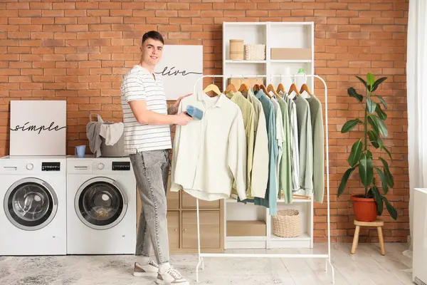 Genç adam evde giysilerini buharlaştırıyor.