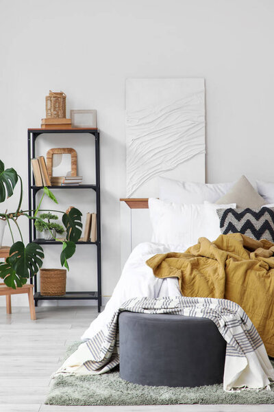 Interior of light bedroom with bookshelf, pouf and painting