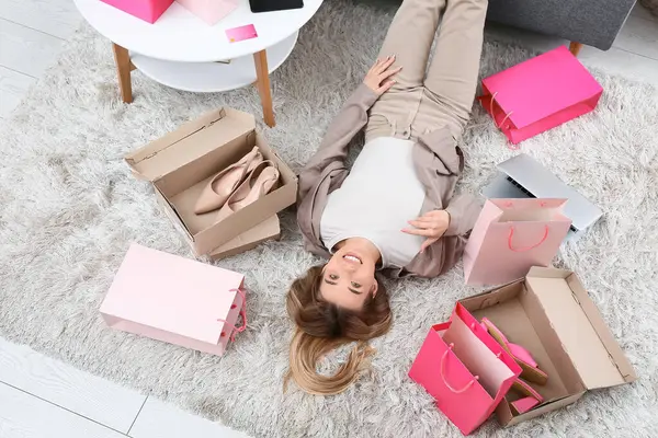 Alışveriş torbalarıyla oturma odasında yerde yatan mutlu genç kadın.