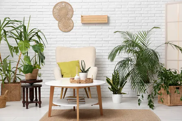 Beyaz tuğla duvarın yanında koltuk, masa ve çiçeklerle dolu bir oda.