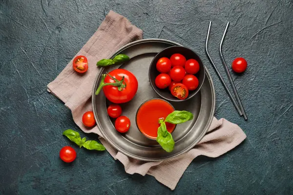 Koyu arkaplanda fesleğen ve sebzeli bir bardak taze domates suyu.