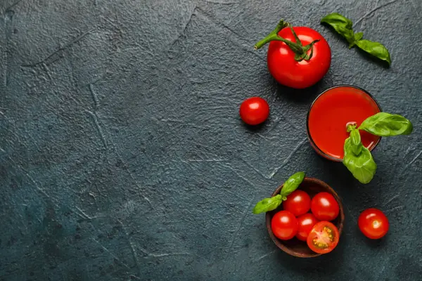 Koyu arkaplanda fesleğen ve sebzeli bir bardak taze domates suyu.