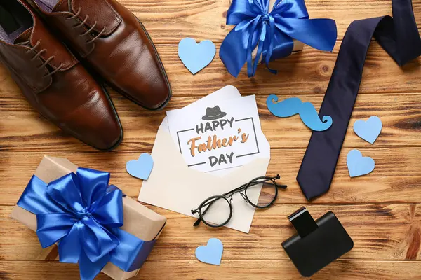 Tahta arka planda Babalar Günü için hediye kutuları, ayakkabılar ve aksesuarlar olan bir kartpostal.