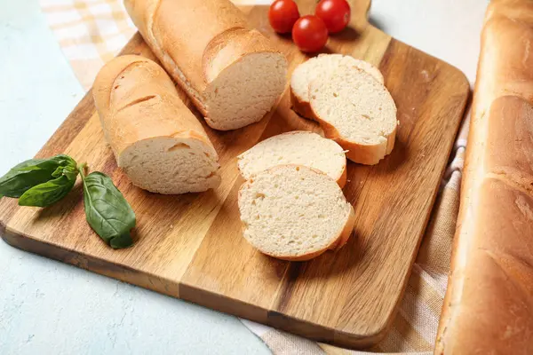 Açık mavi arkaplanda taze baget, fesleğen ve kiraz domatesli ahşap tahta, yakın plan.