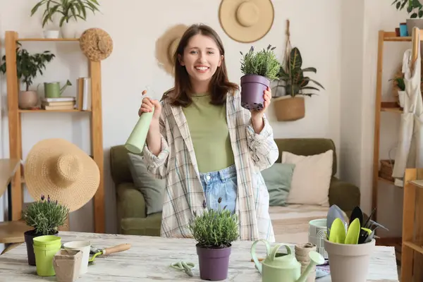 Evde lavanta çiçekleri ve sprey suyu şişesi olan genç bir kadın var.