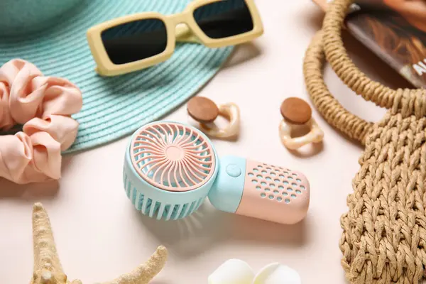 Açık pembe arka planda bayan yaz aksesuarları ve mini fan.