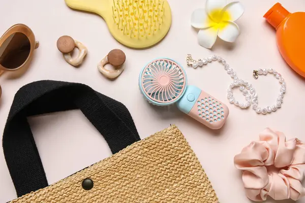 Kadın aksesuarları ve açık pembe arka planda mini fanı olan bir çanta.