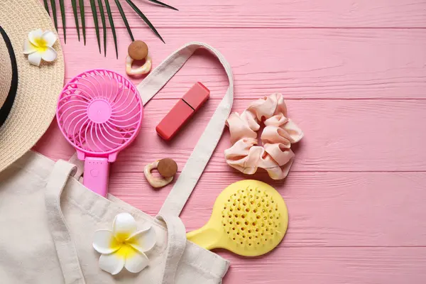 Kadın aksesuarları ve pembe ahşap arka planda mini fanı olan bir çanta.