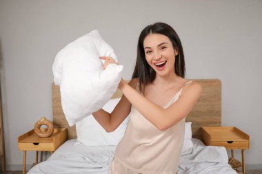Pijamalı, genç ve güzel bir kadın evde yastıklarla savaşıyor.