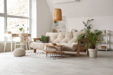 Oturma odasının içinde bej kanepe, kahve masası ve bitkiler.