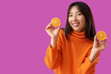 Mor arkaplanda taze portakalları olan genç bir Asyalı kadın.