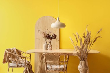 Mutfağın içinde yemek masası, kurumuş çiçekler ve lamba var.