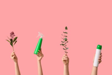 Deterjan şişeleriyle kadın elleri ve pembe arka planda bitki dalları.