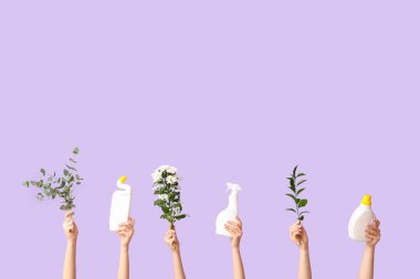 Deterjan şişeleri, çiçekler ve mor arka planda bitki dalları olan birçok kadın eli.