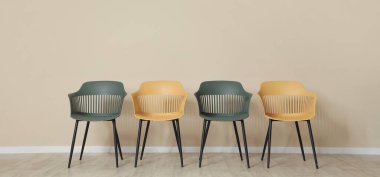 Bej duvarın yanında sarı ve yeşil sandalyeler.