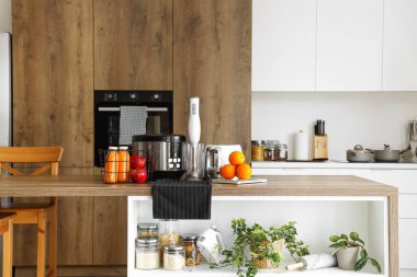 Çoklu fırın, blender, tost makinesi ve portakallı teraziler mutfaktaki ahşap masada.